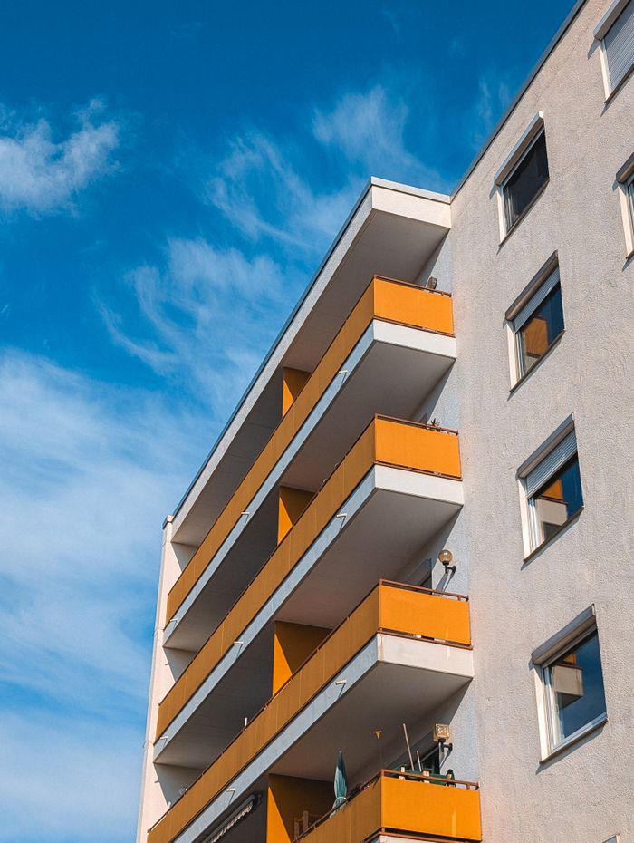 A modern apartment building with distinct orange balconies under a bright blue sky.